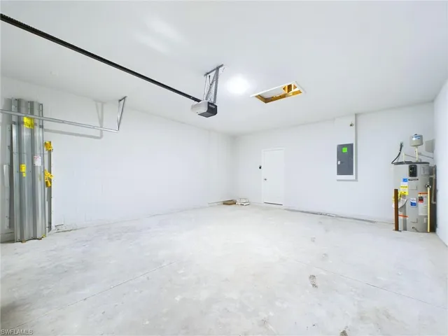 Garage with a garage door opener, electric panel, and water heater