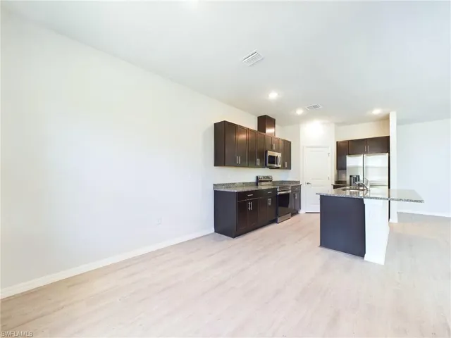 Kitchen featuring a kitchen island with sink, dark brown cabinets, stainless steel appliances, a breakfast bar, and light hardwood / wood-style floors