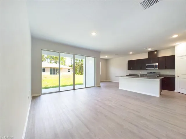 Kitchen with light wood-type flooring, appliances with stainless steel finishes, a center island with sink, and sink