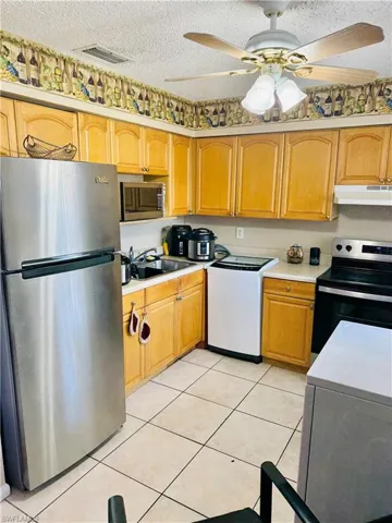 Kitchen featuring stainless steel appliances, light countertops, a ceiling fan, light tile patterned flooring, and a textured ceiling