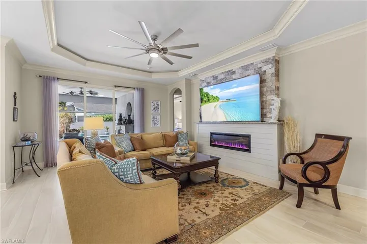 Tray ceiling with a ceiling fan, stone-accented media wall with an integrated electric fireplace, wood-finish flooring, and sliding glass doors to the exterior