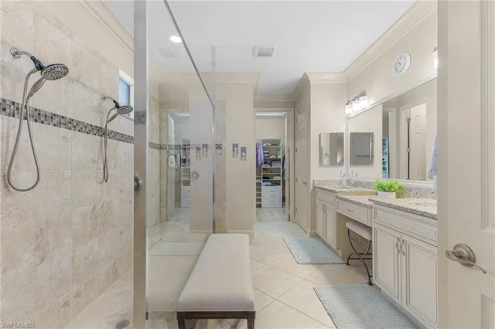 Spacious bathroom featuring a dual vanity with light-colored countertops, large wall-mounted mirror, tiled flooring, and a walk-in shower with dual shower heads and mosaic accent tile