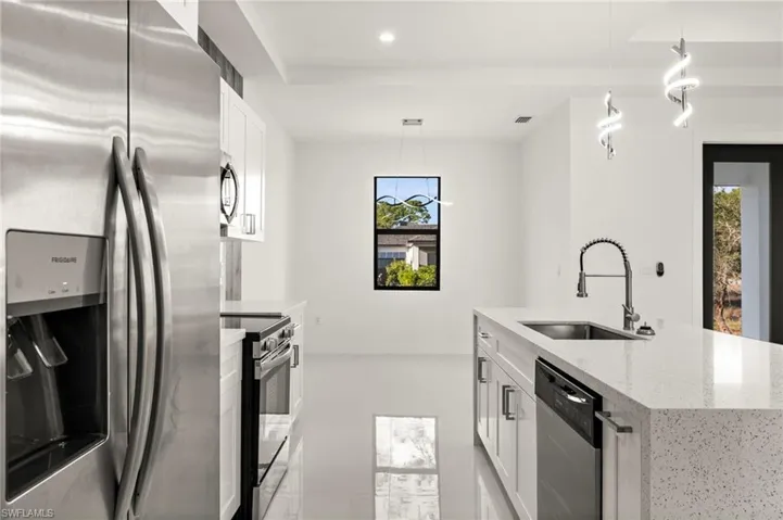 Kitchen with stainless steel appliances, white cabinetry, light stone countertops, decorative light fixtures, and a kitchen island with sink