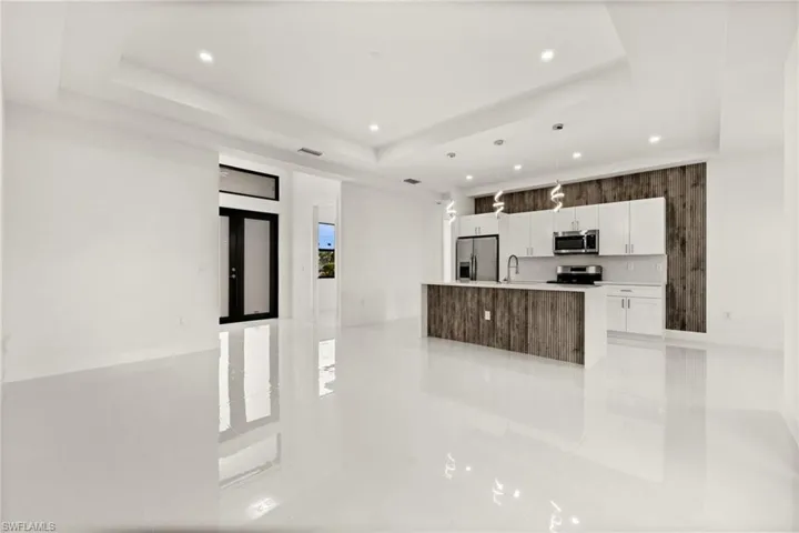 Kitchen featuring stainless steel appliances, open floor plan, decorative light fixtures, white cabinets, and a kitchen island with sink