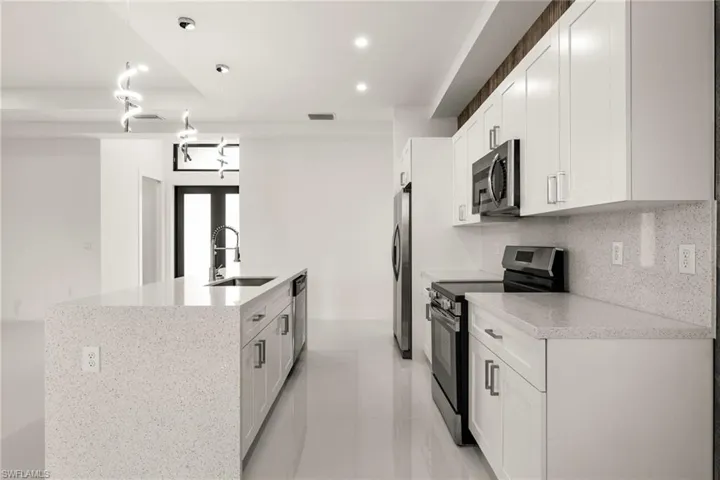 Kitchen featuring stainless steel appliances, white cabinets, an island with sink, and pendant lighting