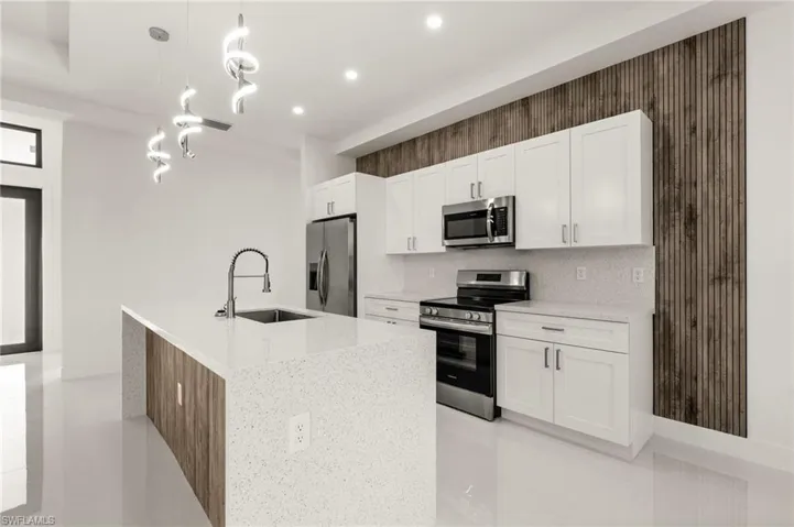 Kitchen featuring stainless steel appliances, light stone counters, a kitchen island with sink, white cabinetry, and wallpapered walls