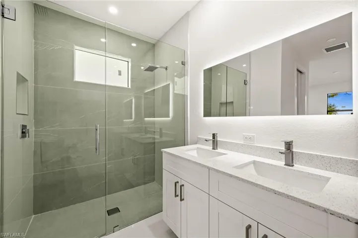 Full bath with double vanity, a shower stall, and recessed lighting