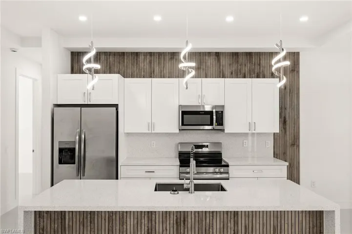 Kitchen with light stone counters, stainless steel appliances, and pendant lighting