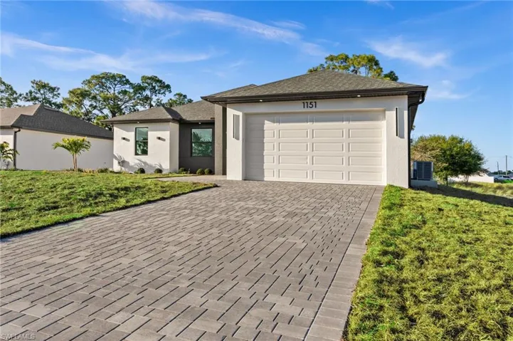 Ranch-style house with stucco siding, decorative driveway, an attached garage, and a front lawn