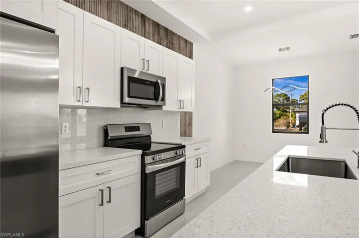 Kitchen with stainless steel appliances, white cabinetry, light stone countertops, hanging light fixtures, and tasteful backsplash