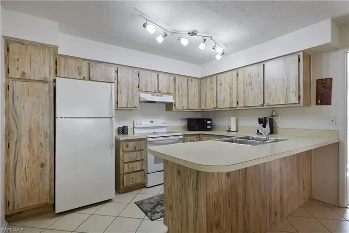 Kitchen featuring white appliances, light tile patterned floors, a peninsula, a textured ceiling, and light countertops