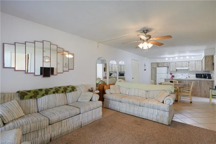 Living area with light tile patterned flooring, light carpet, ceiling fan, and arched walkways