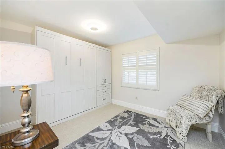 This room features light-colored carpeting, a window with white louvered shutters, and built-in white cabinetry with drawers and handles
