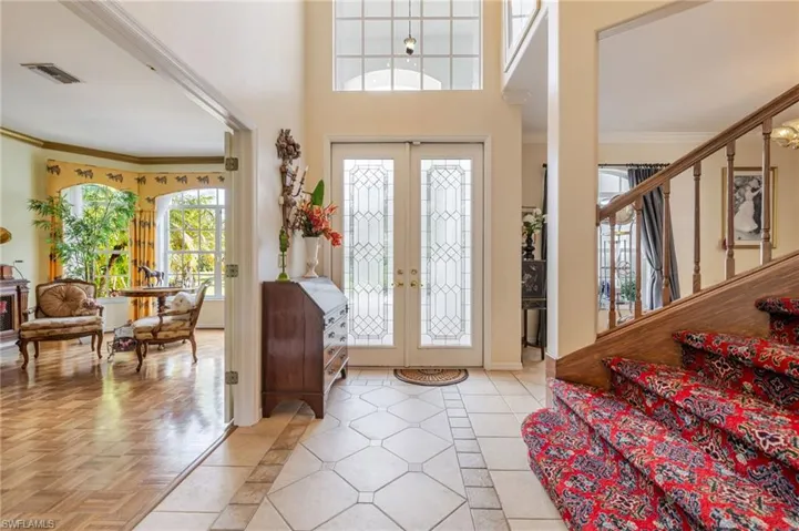 Entryway featuring crown molding, french doors, light tile patterned floors, inlaid floor details, and a high ceiling
