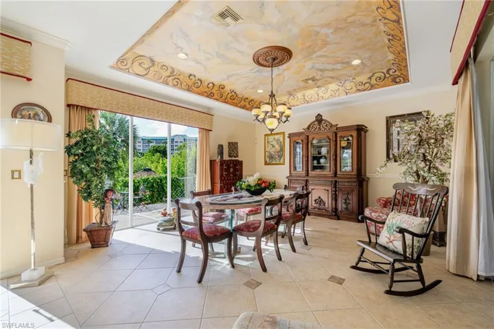 Dining area with a raised ceiling, crown molding, a chandelier, and light tile patterned floors