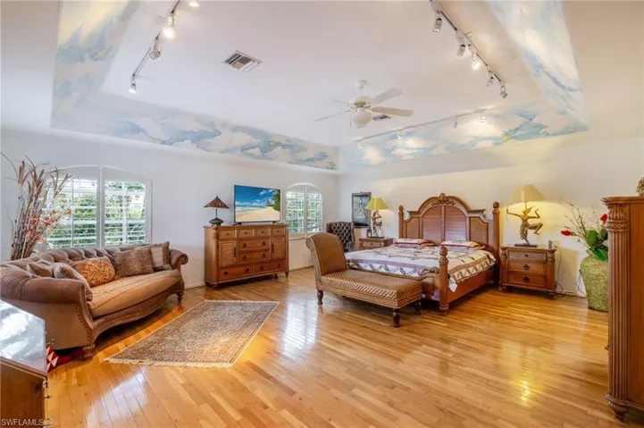 Bedroom with track lighting, a raised ceiling, light wood-style floors, and ceiling fan