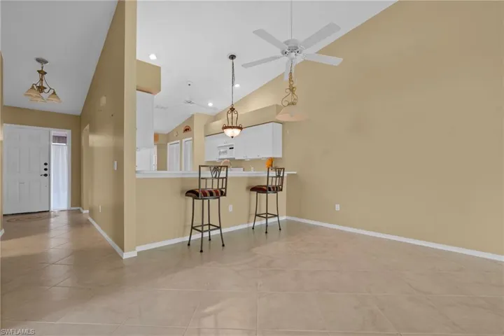 Open concept living area featuring vaulted ceilings, tile flooring, a breakfast bar, and a ceiling fan