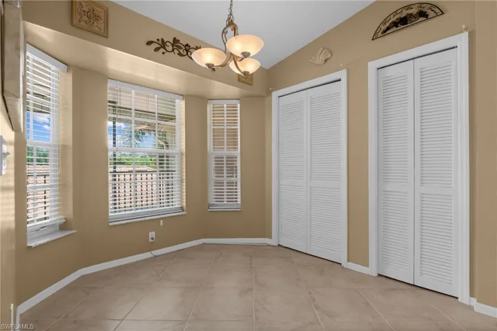 Tiled flooring throughout this space, featuring multiple windows with blinds, a ceiling-mounted light fixture, and two louvered bifold closet doors
