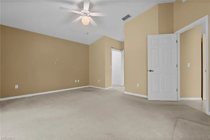 Spacious room featuring vaulted ceilings, light-toned carpeting, and a ceiling fan with integrated lighting