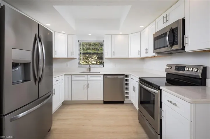Kitchen with stainless steel appliances, white cabinetry, recessed lighting, a tray ceiling, and light wood finished floors