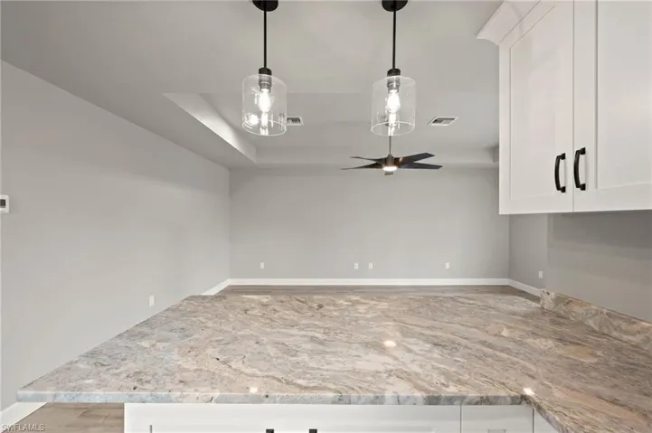 Kitchen with white cabinets, hanging light fixtures, light stone counters, and ceiling fan