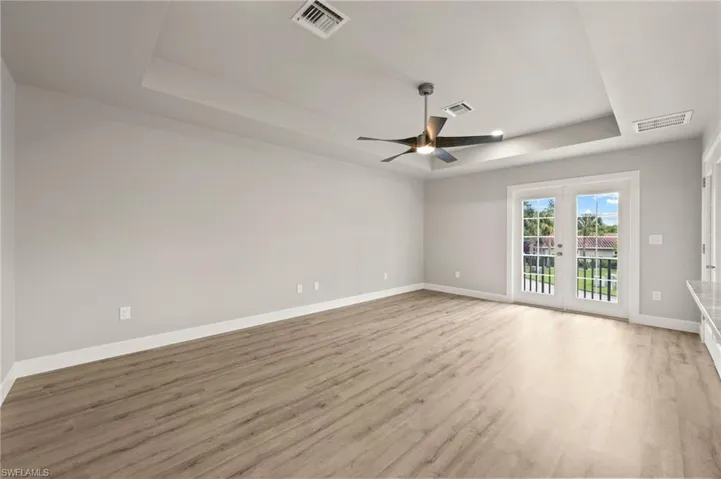 Unfurnished room with ceiling fan, light wood-type flooring, and a tray ceiling