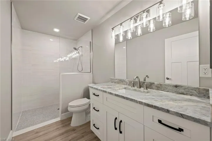 Bathroom with hardwood / wood-style floors, vanity, a tile shower, and toilet