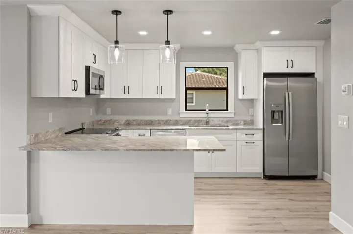 Kitchen with white cabinetry, decorative light fixtures, stainless steel appliances, sink, and light hardwood / wood-style floors