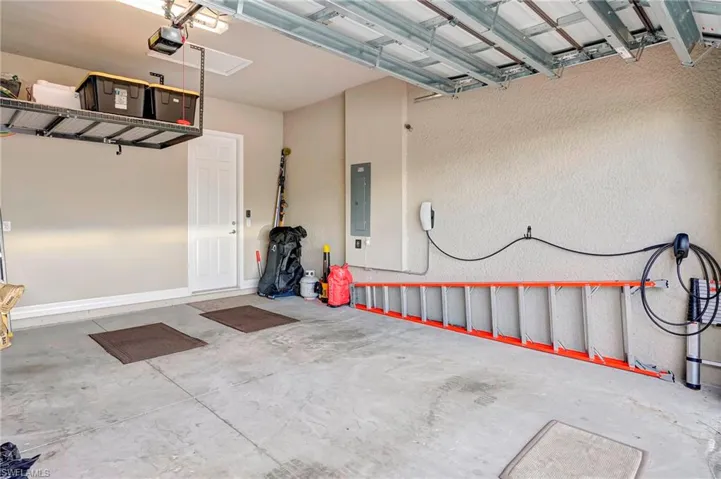 Garage featuring a garage door opener and electric panel with Tesla charger