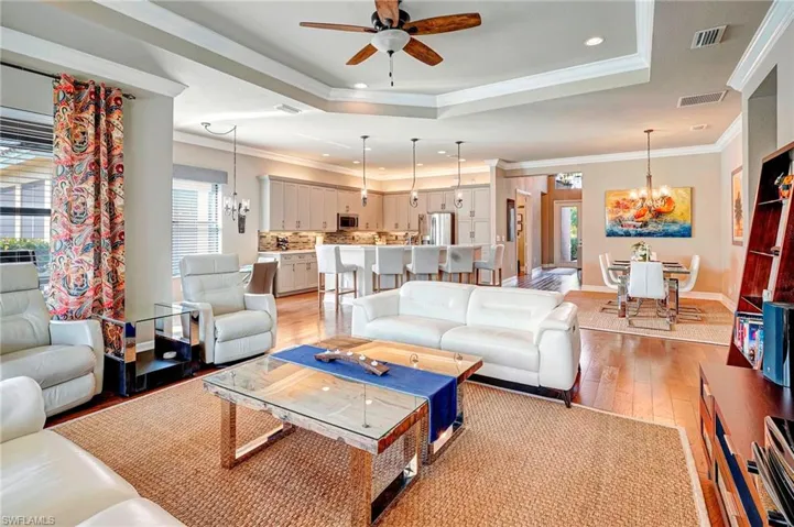 Living room featuring ceiling fan with notable chandelier, crown molding, light hardwood / wood-style floors, and a raised ceiling