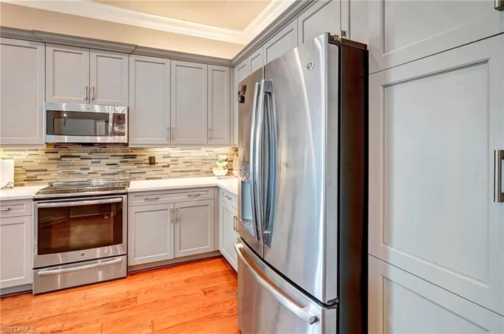 Kitchen featuring light wood-type flooring, appliances with stainless steel finishes, ornamental molding, and tasteful backsplash
