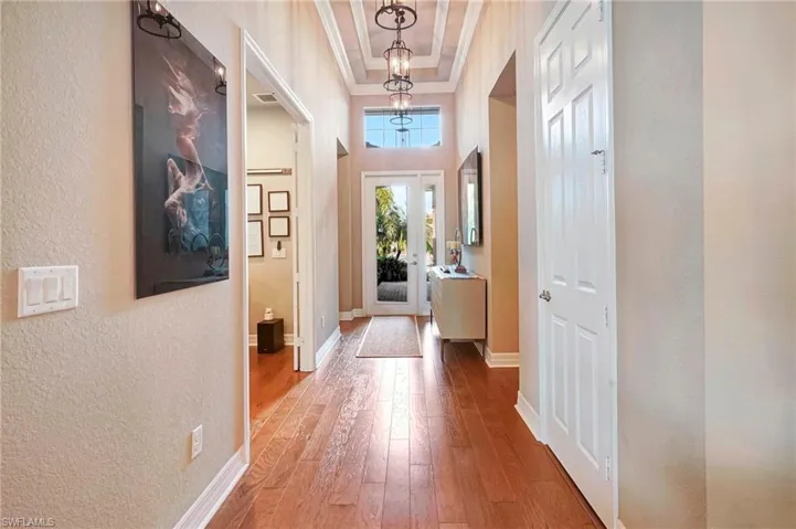 Entryway with wood-type flooring, a towering ceiling, a chandelier, a raised ceiling, and ornamental molding