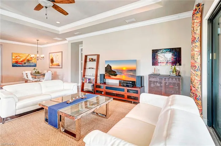Living room with ceiling fan with notable chandelier, crown molding, and a tray ceiling