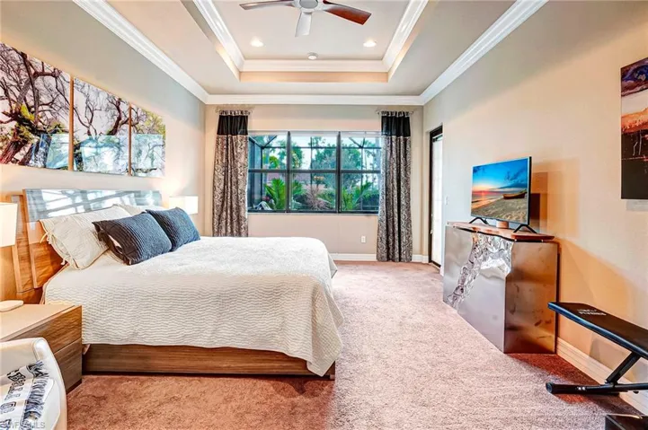 Carpeted bedroom featuring a tray ceiling, ornamental molding, and ceiling fan