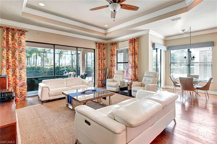 Living room with hardwood / wood-style floors, a tray ceiling, ceiling fan with notable chandelier, and ornamental molding