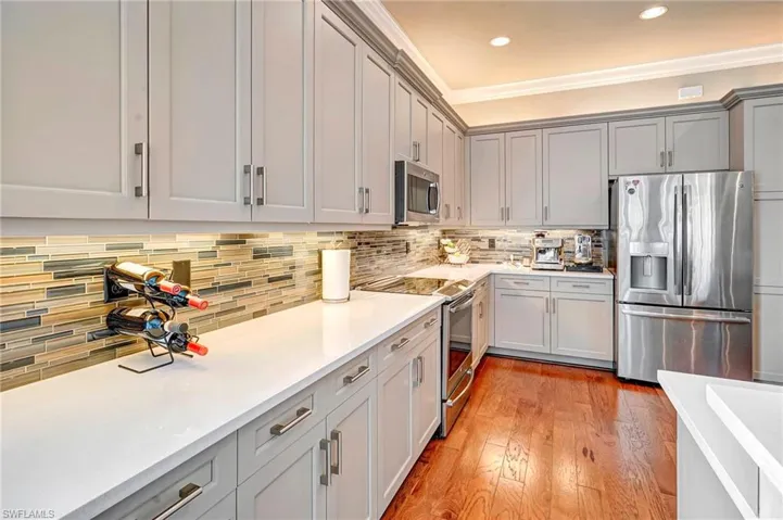 Kitchen featuring gray cabinetry, light hardwood / wood-style floors, crown molding, stainless steel appliances, and decorative backsplash