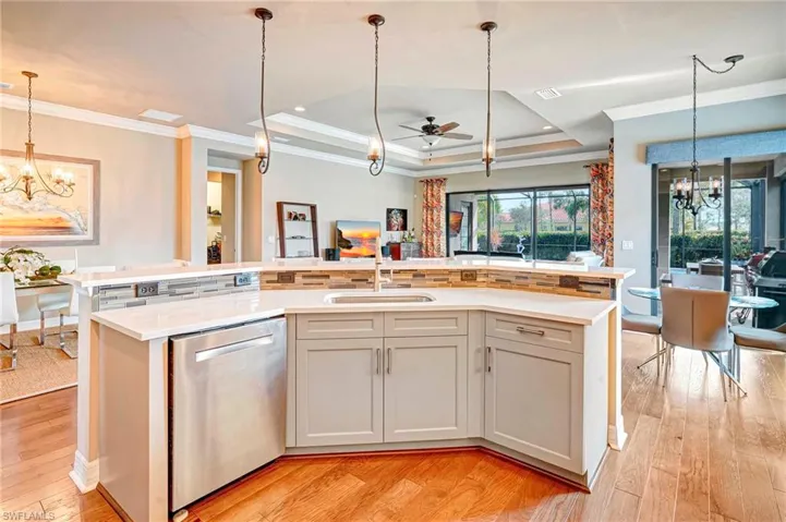 Kitchen featuring white cabinets, dishwasher, a raised ceiling, and a kitchen island with sink