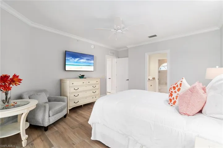 Bedroom featuring ornamental molding, wood finished floors, ensuite bath, and a ceiling fan