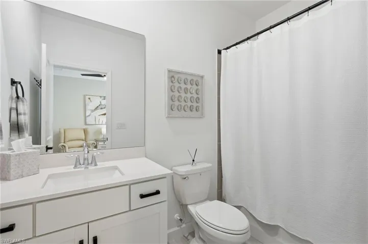 Modern bathroom featuring a white vanity with dual drawers and black hardware, white quartz countertop, chrome faucet, large illuminated mirror, white subway tile surround, and a separate toilet with white shower curtain enclosure