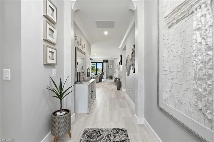 Bright hallway showcasing light wood-finish flooring, white shiplap accent wall, recessed ceiling lighting, and framed wall art