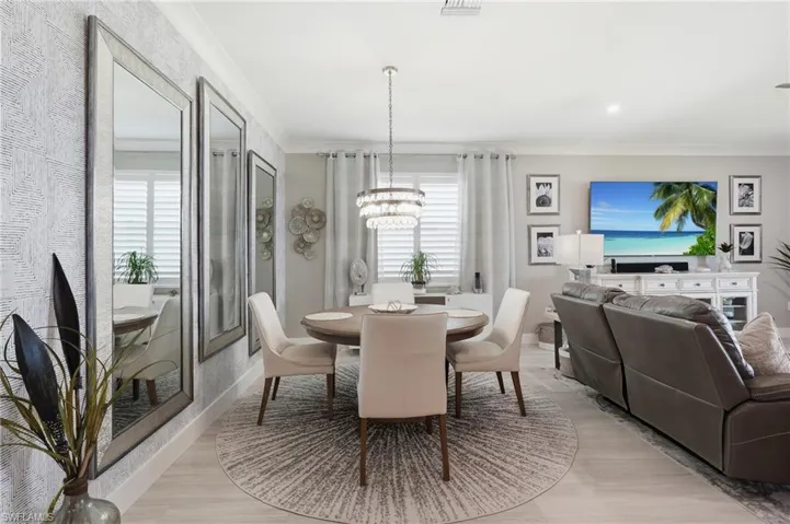Open-concept living space featuring a round pedestal dining table, neutral upholstered seating, light wood-finish flooring, and a circular area rug anchoring the dining zone