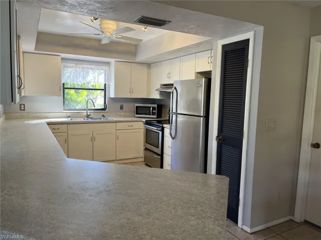 Kitchen featuring sink, ceiling fan, a tray ceiling, kitchen peninsula, and stainless steel appliances