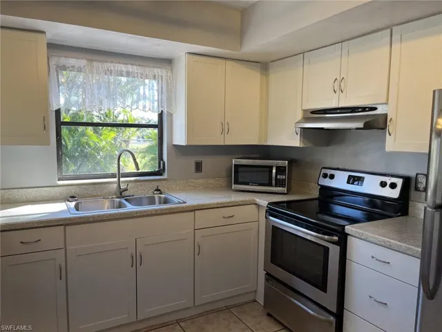 Kitchen with white cabinets, light tile patterned floors, stainless steel appliances, and sink