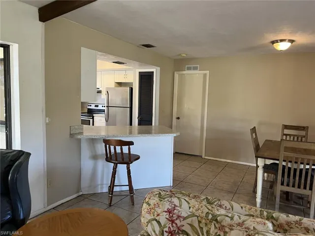 Kitchen featuring kitchen peninsula, light tile patterned floors, electric range, white cabinets, and stainless steel refrigerator