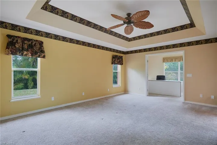 Carpeted spare room with ceiling fan, baseboards, and a tray ceiling