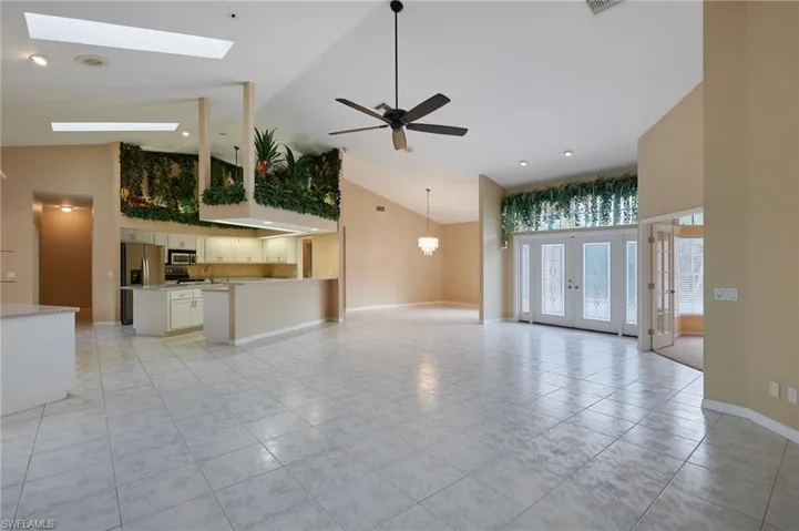 Unfurnished living room featuring high vaulted ceiling, light tile patterned floors, ceiling fan, baseboards, and a skylight