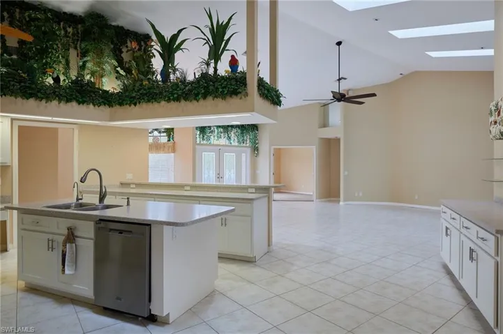Kitchen featuring stainless steel dishwasher, a sink, a center island with sink, a skylight, and light tile patterned flooring