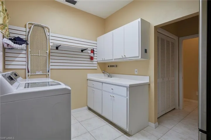 Laundry room featuring washing machine and dryer, cabinet space, light tile patterned flooring, and baseboards