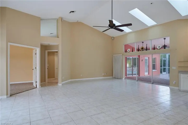 Spare room featuring high vaulted ceiling, light tile patterned flooring, a skylight, ceiling fan, and baseboards