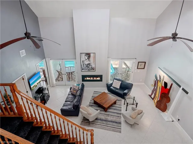 Living room with tile patterned flooring, french doors, ceiling fan, and a towering ceiling